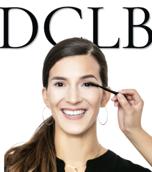 A smiling guest having her lashes brushed, with the DCLB wordmark behind her